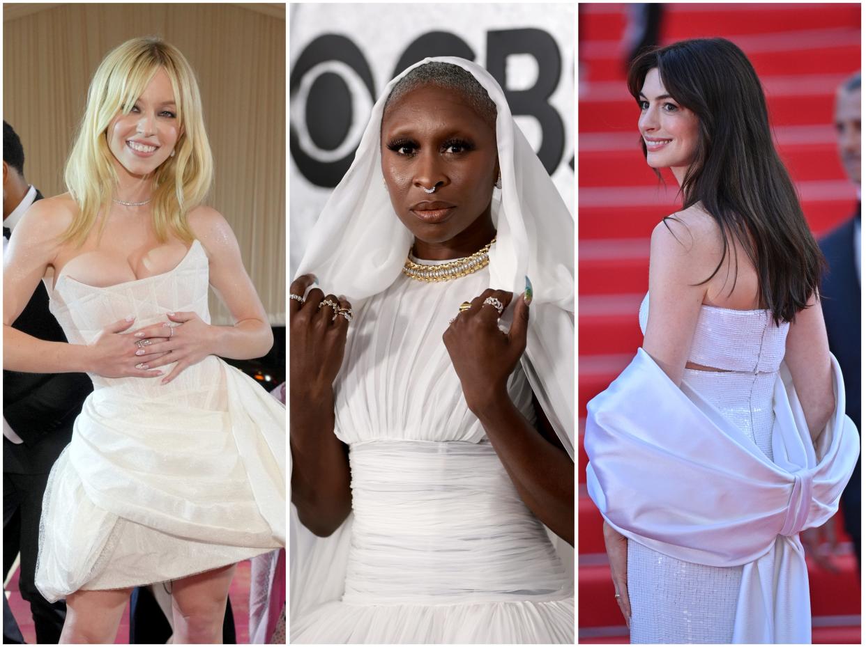 Sydney in a white strapless minidress with exposed corset detailing and a wide skirt. Cynthia with her hands on a white veil-looking cloak on her white tulle gown. Anne turned to the back showing a white two-piece look with a dramatic bow-shaped shawl.