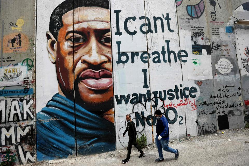 People walk past a mural showing the face of Floyd painted on a section of Israel's controversial separation barrier in Bethlehem on March 31, 2021.<span class="copyright">Emmanuel Dunand—AFP/Getty Images</span>