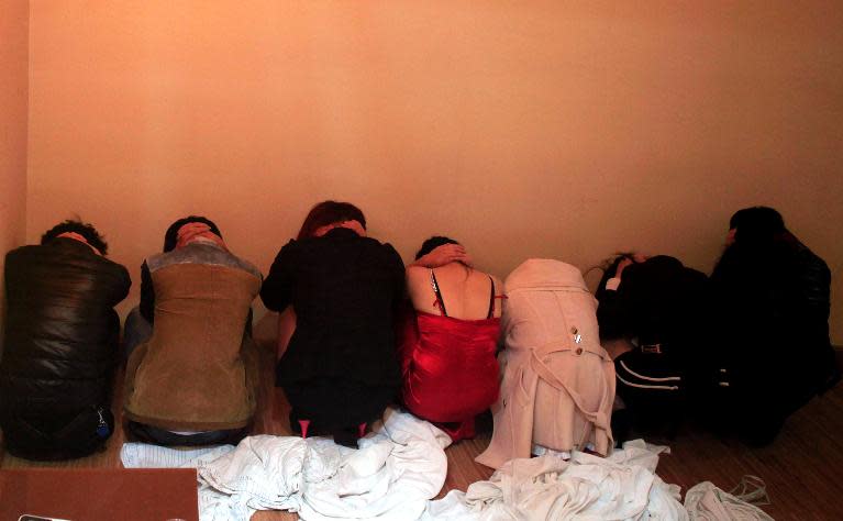 Suspects crouch by a wall during a police raid on an entertainment center in Dongguan, China's Guangdong province on February 9, 2014