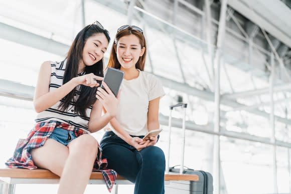 Two young Chinese women giggle over their smartphones.