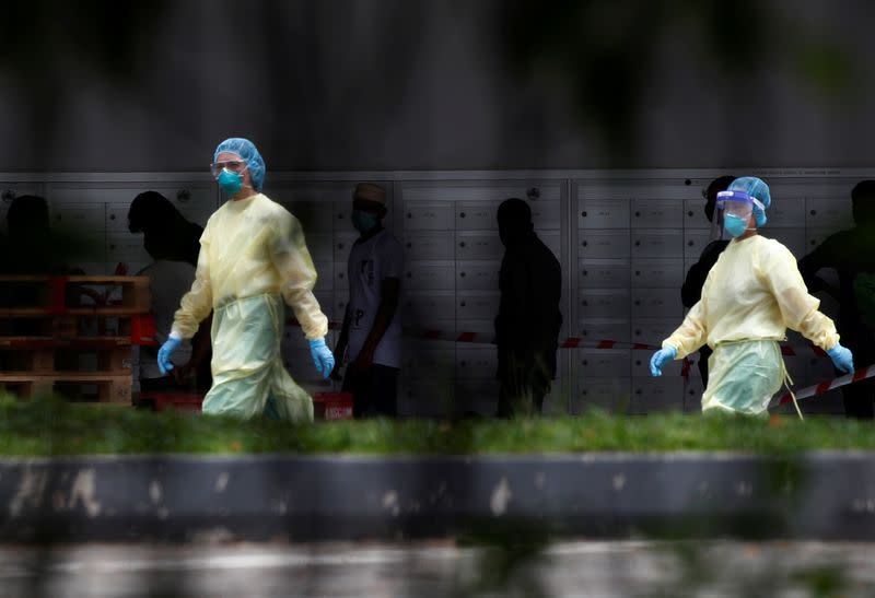 Medical personnel walk past migrant workers at a dormitory during the coronavirus (COVID-19) outbreak in Singapore