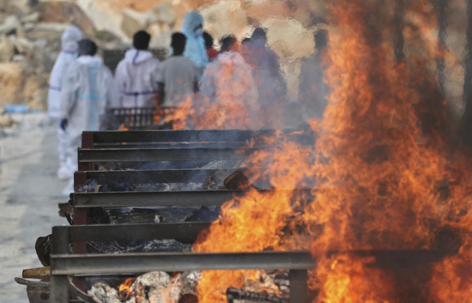 Family members perform last rites of a person who died of COVID-19 as funeral pyres of other victims burn at an open crematorium set up at a granite quarry on the outskirts of Bengaluru, India, Wednesday, May 5, 2021. (AP Photo/Aijaz Rahi)