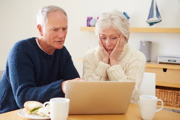 A worried senior couple examining Medicare plan costs on their laptop.