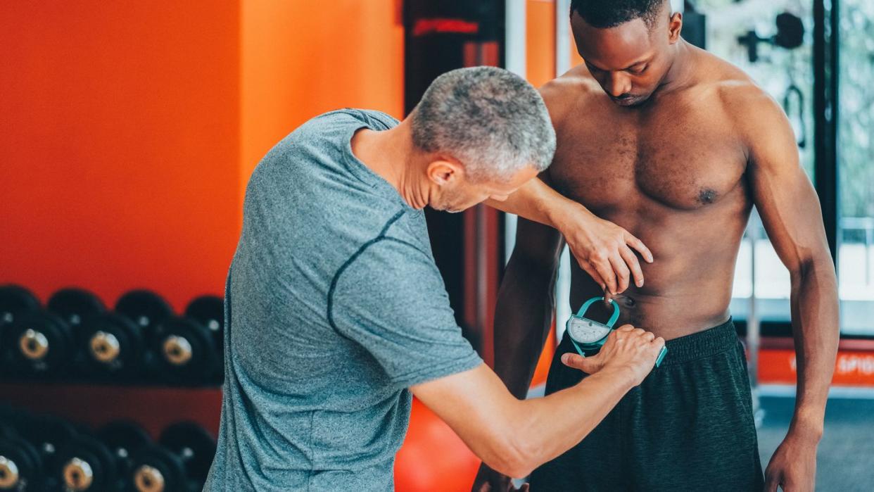 coach measuring client's body fat with caliper