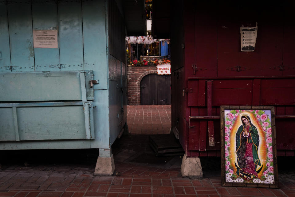 A framed painting depicting Our Lady of Guadalupe is propped against a shuttered market stall on empty Olvera Street in downtown Los Angeles, Wednesday, Dec. 16, 2020. Olvera Street, known as the birthplace of Los Angeles, has been particularly hard hit by the coronavirus pandemic, with shops and restaurants closed and others barely hanging on. (AP Photo/Jae C. Hong)