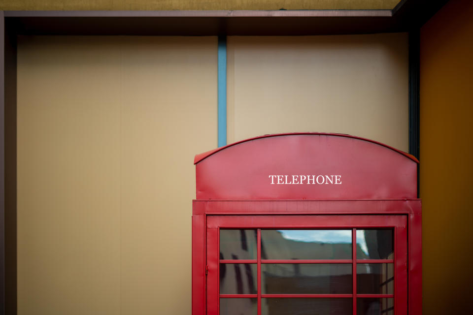 Partial view of a classic British red telephone booth with "TELEPHONE" sign, against a plain backdrop