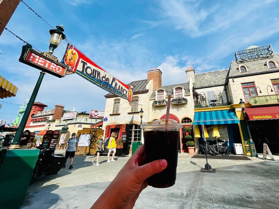 Holding a coffee in front of a row of Universal shops