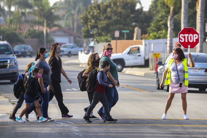 FOUNTAIN VALLEY, CA - SEPTEMBER 23: A crossing guard help cross the street as students return, after months of closure due COVID-19 pandemic, at James H Cox Elementary School on Wednesday, Sept. 23, 2020 in Fountain Valley, CA. (Irfan Khan / Los Angeles Times)