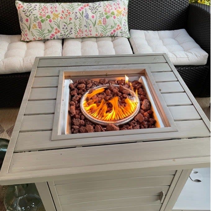 Patio fire pit table with lit flame, surrounded by lava rocks, next to outdoor furniture