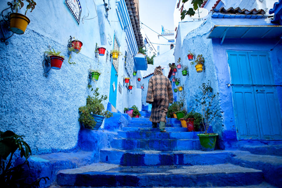 Man walks up the blue steps of a narrow street in the blue-washed Chefchaouen, Morocco. This town is known for being painted in exclusively one color (blue).