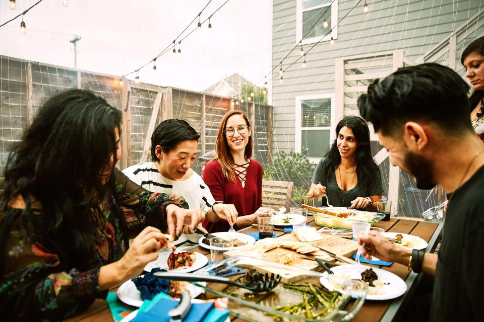 Smiling and laughing friends sharing dinner at table in backyard