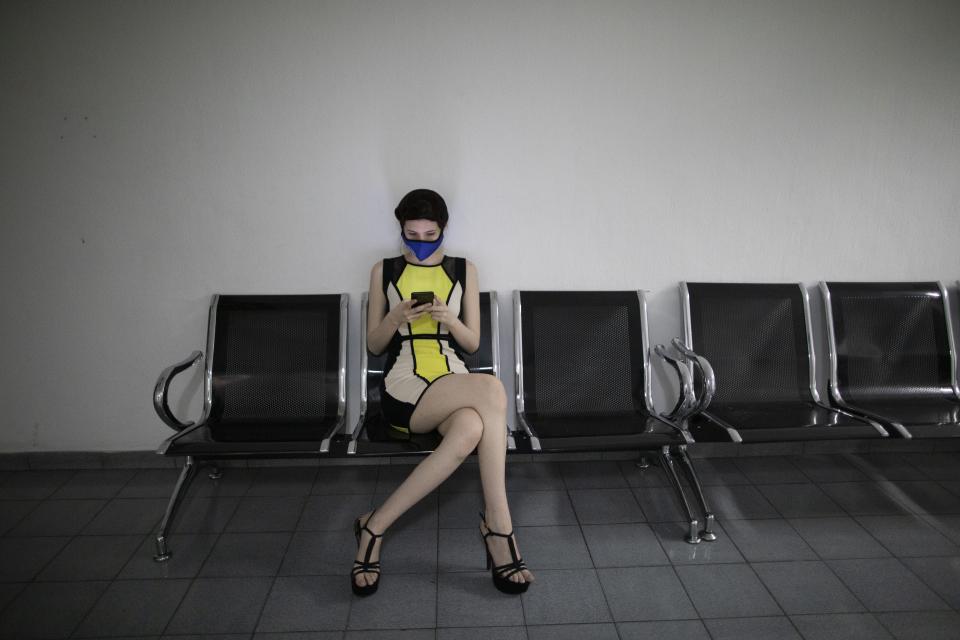 Monagas state beauty pageant contestant Maria Antonietta Silva, wearing a protective face mask, passes the time with her phone while waiting for makeup, at the Venevision television station, in Caracas, Venezuela, Friday, Sept. 18, 2020. Quarantine rules and social distancing has forced the contestants to train at home and online with limited access to the venue itself where strict measures are in place. The Miss Venezuela pageant is due to take place on Sept. 24. (AP Photo/Ariana Cubillos)