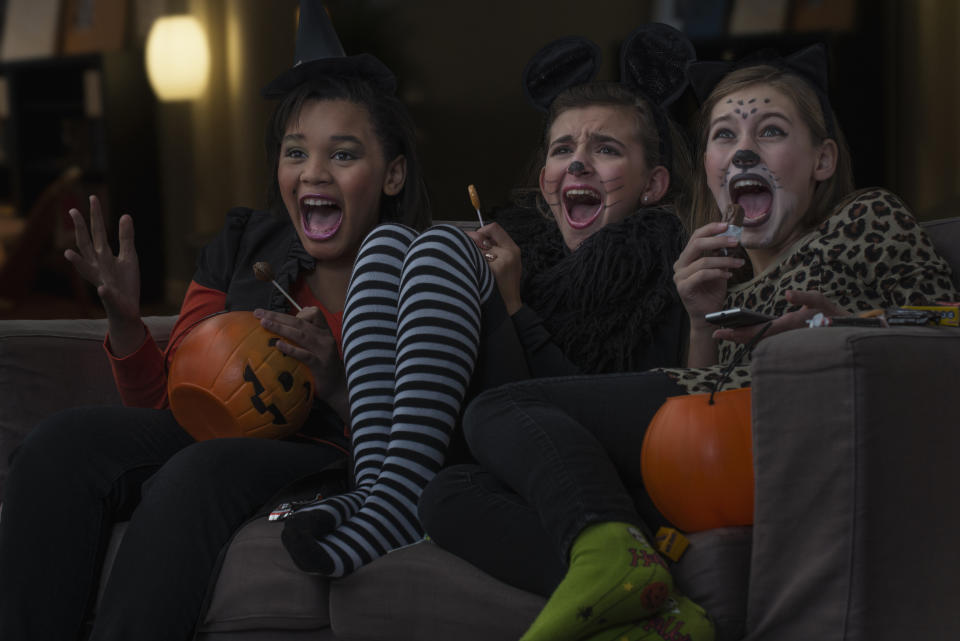 Girls in costumes watching scary movie together on Halloween