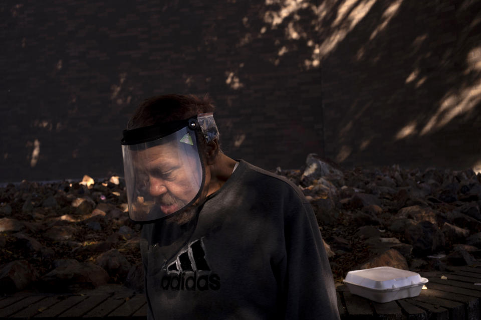 A man wearing a face shield walks through a shaft of light past a police station in the Skid Row area of Los Angeles, Wednesday, Nov. 22, 2023. (AP Photo/Jae C. Hong)