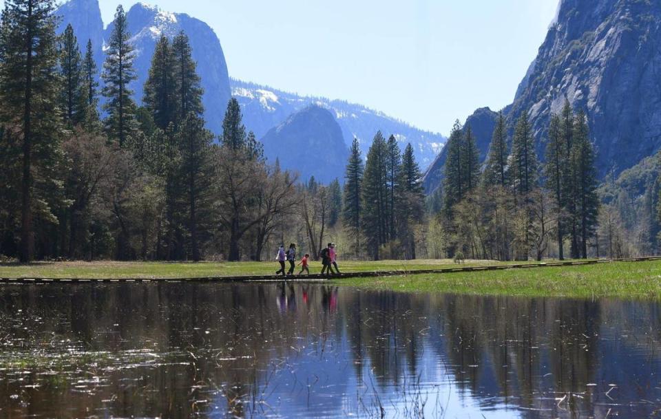 A family walks on a boardwalk through a flooded Sentinel Meadow Friday, April 28, 2023 in Yosemite Valley.