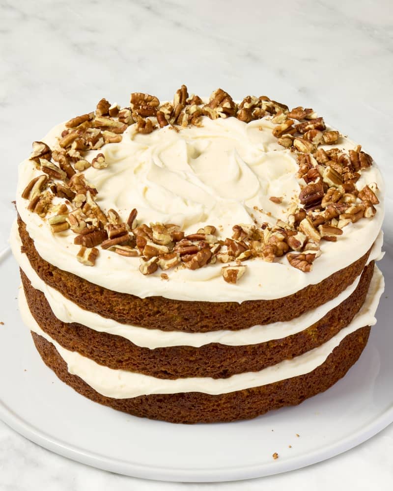 shot of a full carrot cake on a white cake plate.