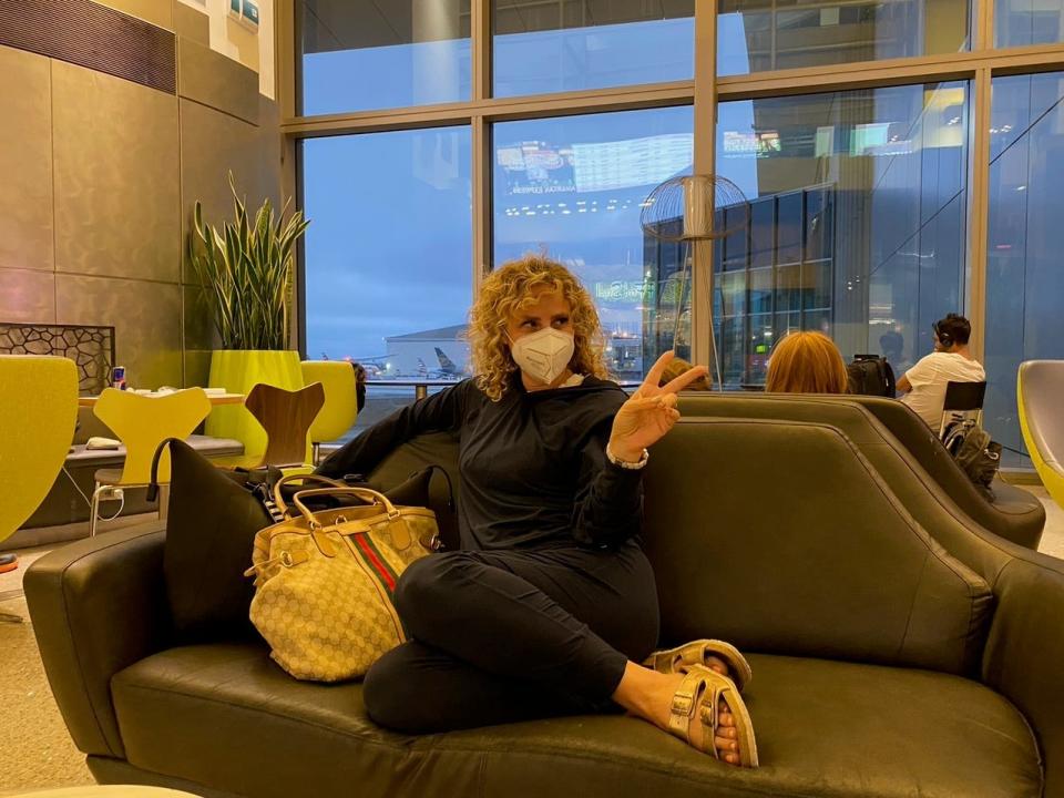 A woman flashing a peace sign wearing a mask, sitting on a couch.