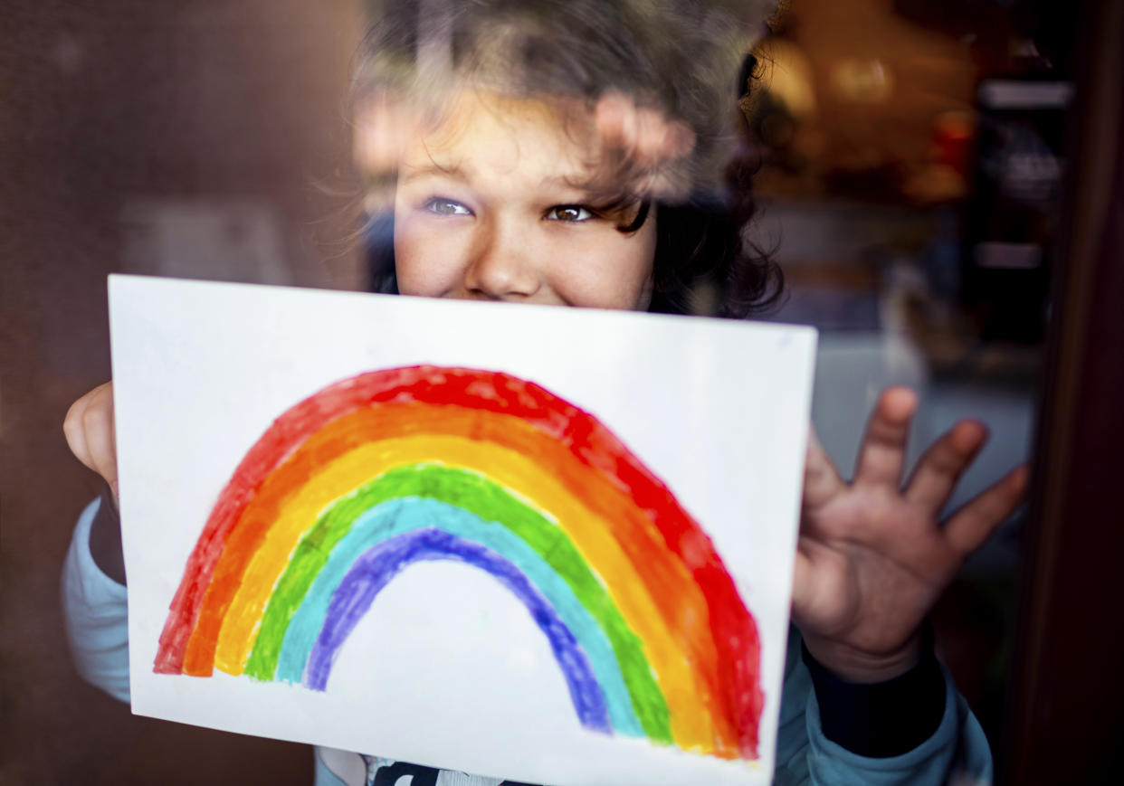 Close up of a little boy putting his rainbow painting on the window during Covid-19