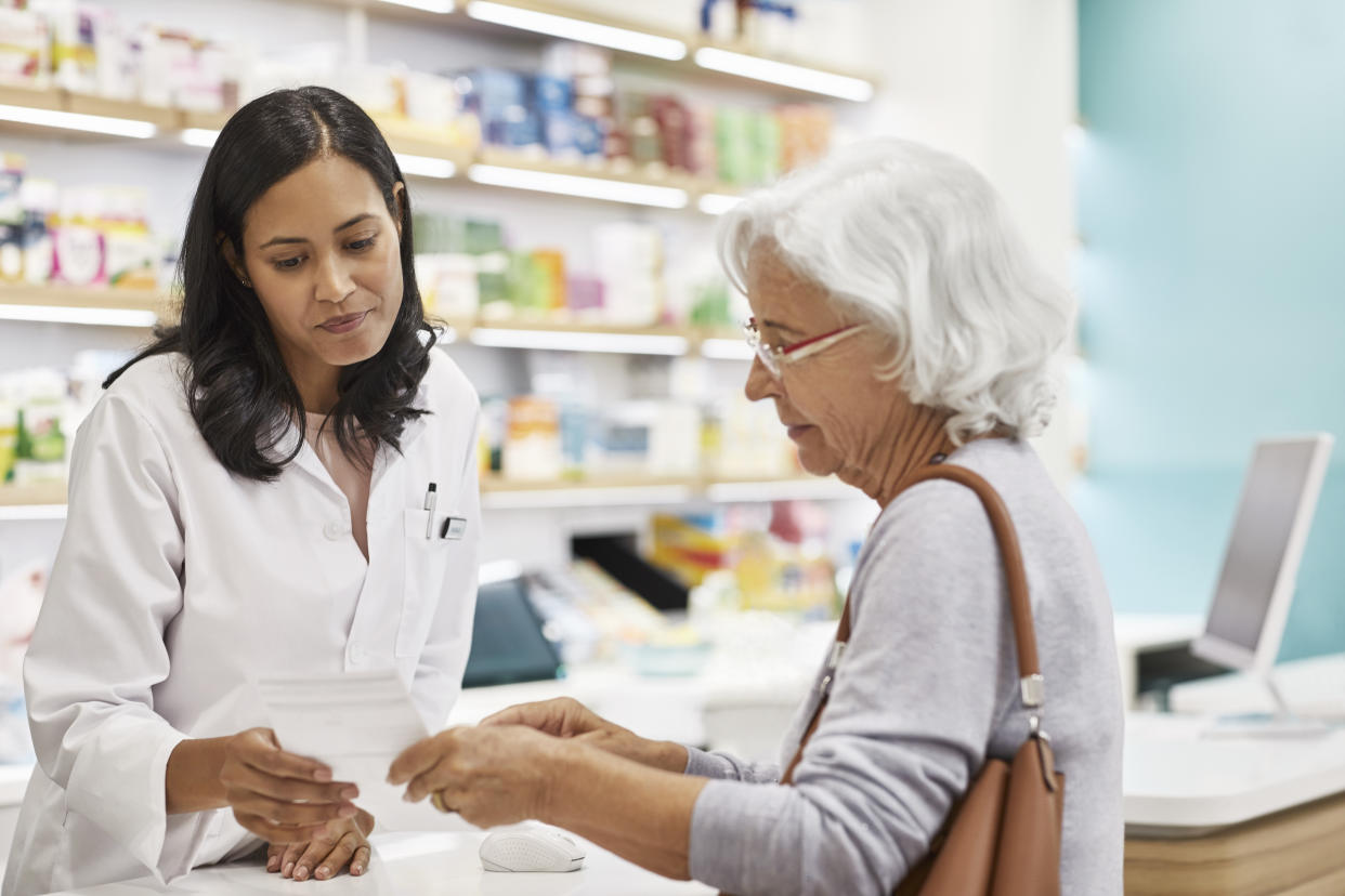 Senior customer showing prescription to female doctor. Cashier is assisting elderly woman at checkout counter. They are standing at pharmacy.