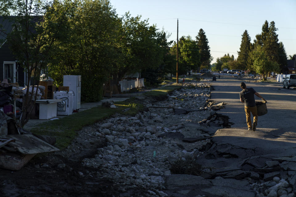 A resident carries out damaged items from his flooded home along a washed out street in Red Lodge, Mont., Wednesday, June 15, 2022. (AP Photo/David Goldman)