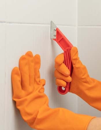 A close up of an orange-gloved-hand using a red tool to regrout tiles.