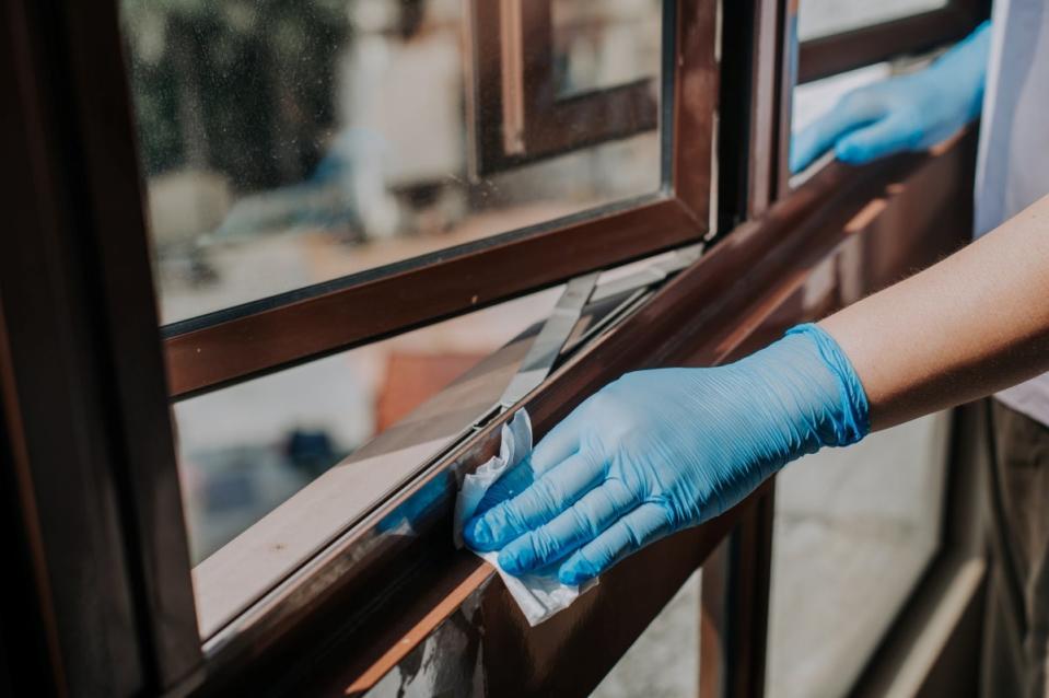 Person wearing blue disposable gloves cleaning windowsills with a wipe.