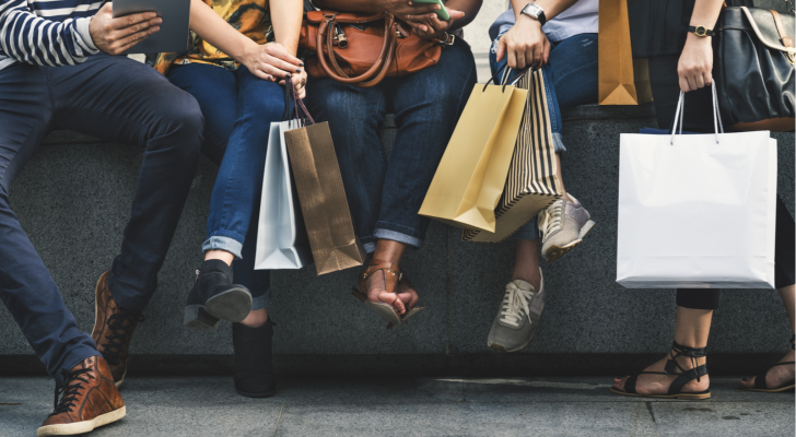 Friends sit on a ledge with shopping bags after shopping retail stores.