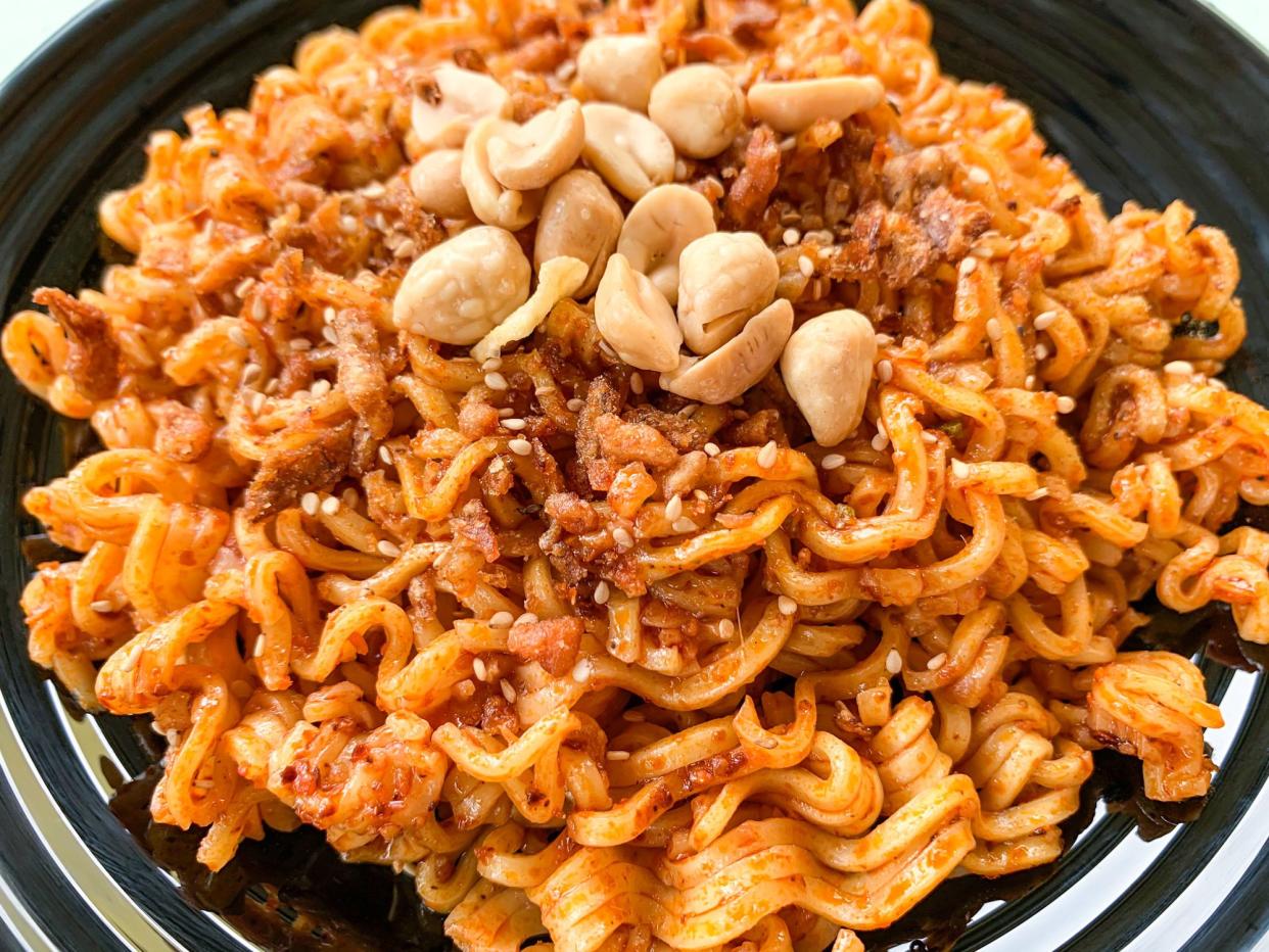 Indonesia instant fried noodle with toppings sesame seeds and peanuts on a plate. Closeup view.