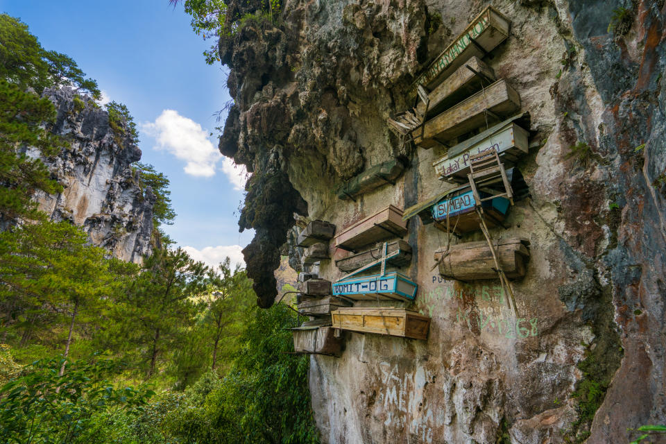Wiew showing hanging coffins in the rock mountain and trees can be seen on the background. 