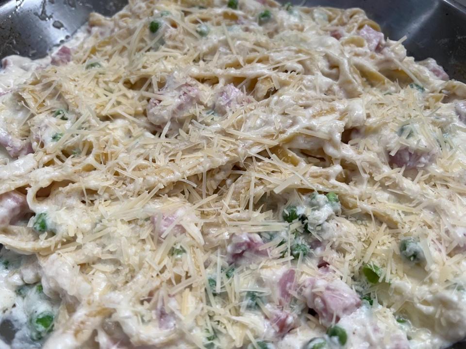 Sprinkled cheese on top of saucy noodles with peas and ham.