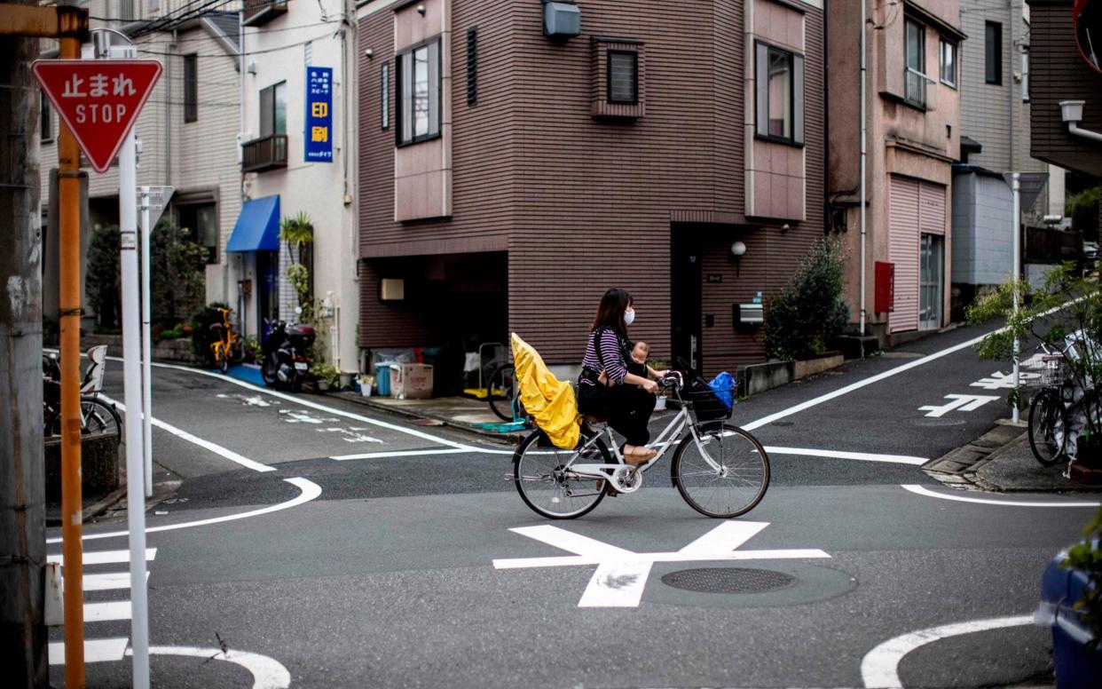 A masked woman cycles across junction with a small child between her legs - Behrouz Mehri/AFP