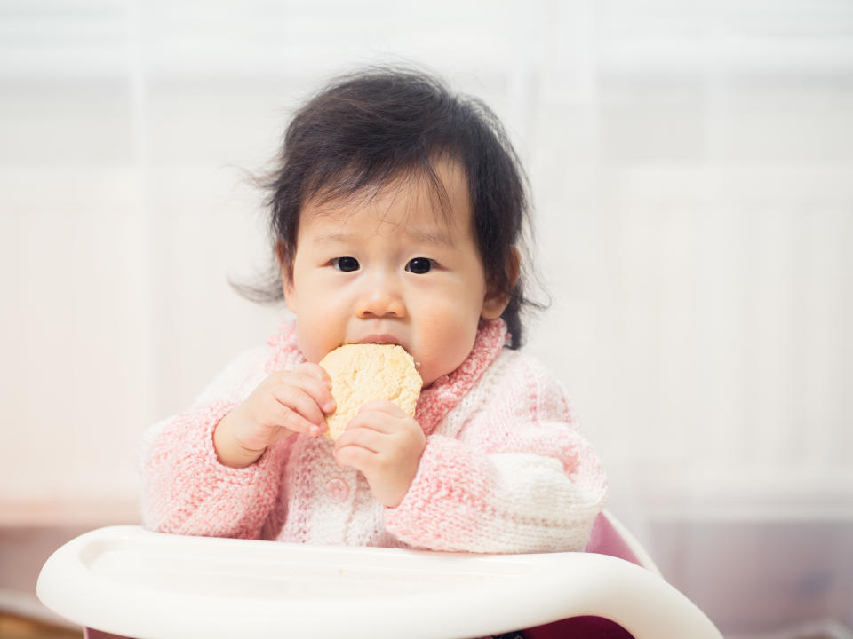 Asian baby girl eating rusk for snack