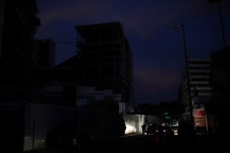 The lights of a car illumine people on the side of the street during a blackout in Caracas