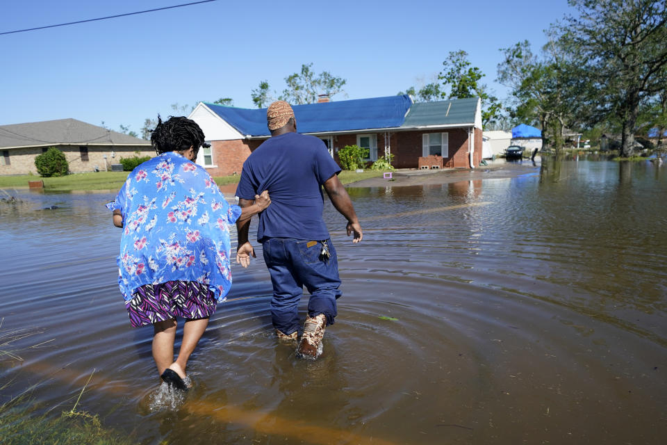 FILE - Soncia King holds onto her husband Patrick King in Lake Charles, La., Saturday, Oct. 10, 2020, as they walk through the flooded street to their home, after Hurricane Delta moved through on Friday. In the past year, the southwestern Louisiana city of Lake Charles weathered two hurricanes, intense rainfall that sent water gushing down streets and a deep freeze that burst pipes. Under a revamped federal flood insurance program rolled out in the fall of 2021, millions of homeowners are set for rate hikes that officials say more accurately reflect a property’s risk. (AP Photo/Gerald Herbert, File)