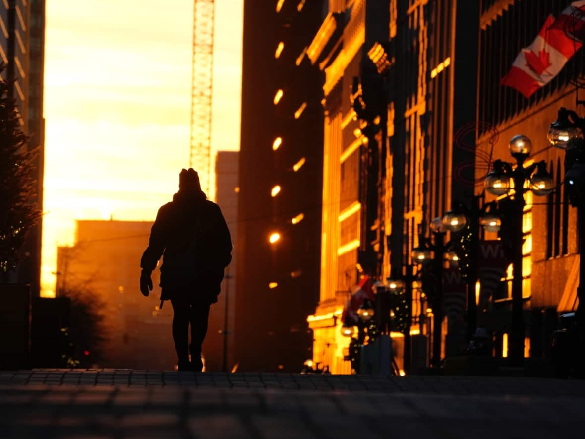 A person walks through Ottawa's downtown core as buildings are lit up by the setting sun on Dec. 3, 2021. (Adrian Wyld/The Canadian Press - image credit)