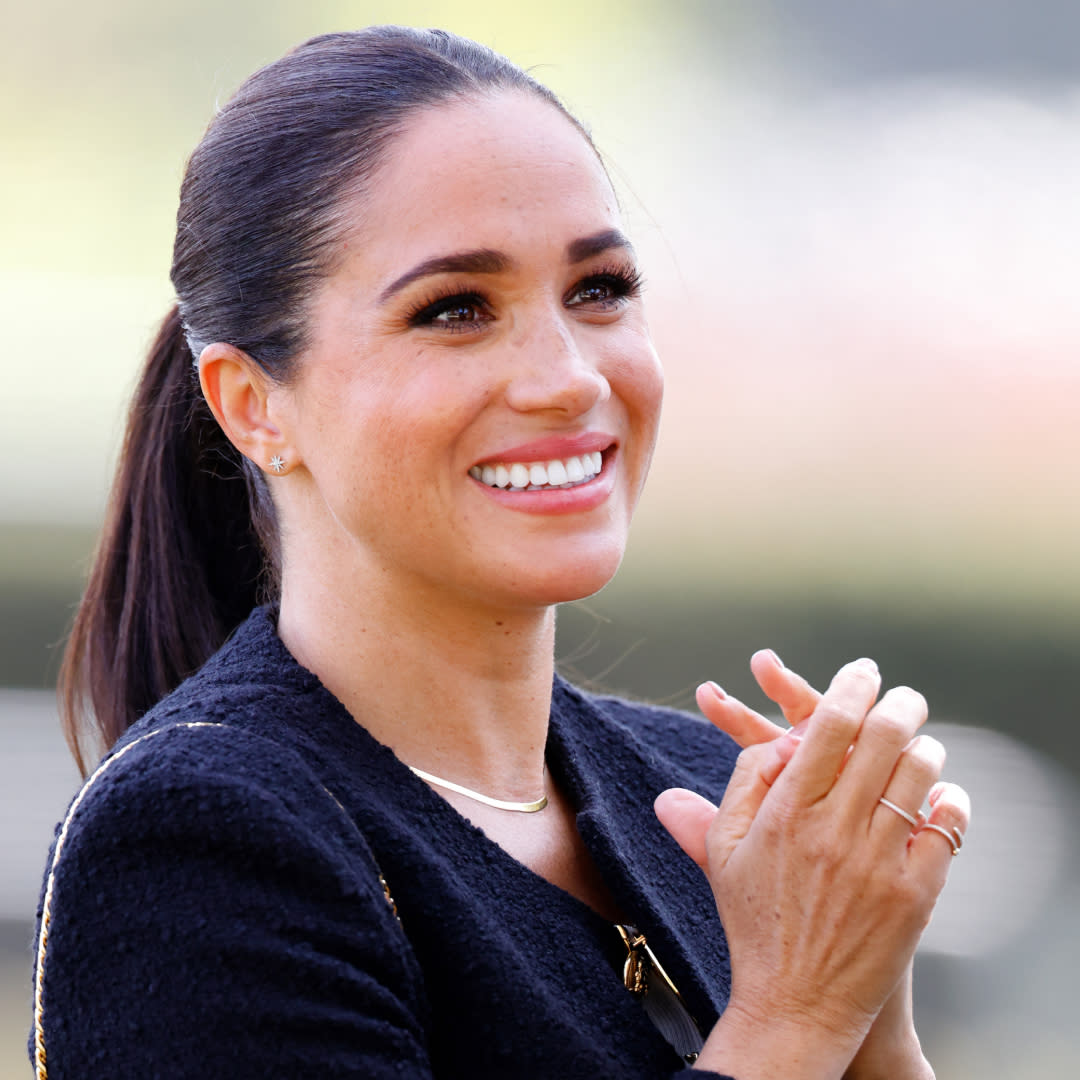  Meghan Markle at an event wearing a collarless jacket tshirt and jeans. 