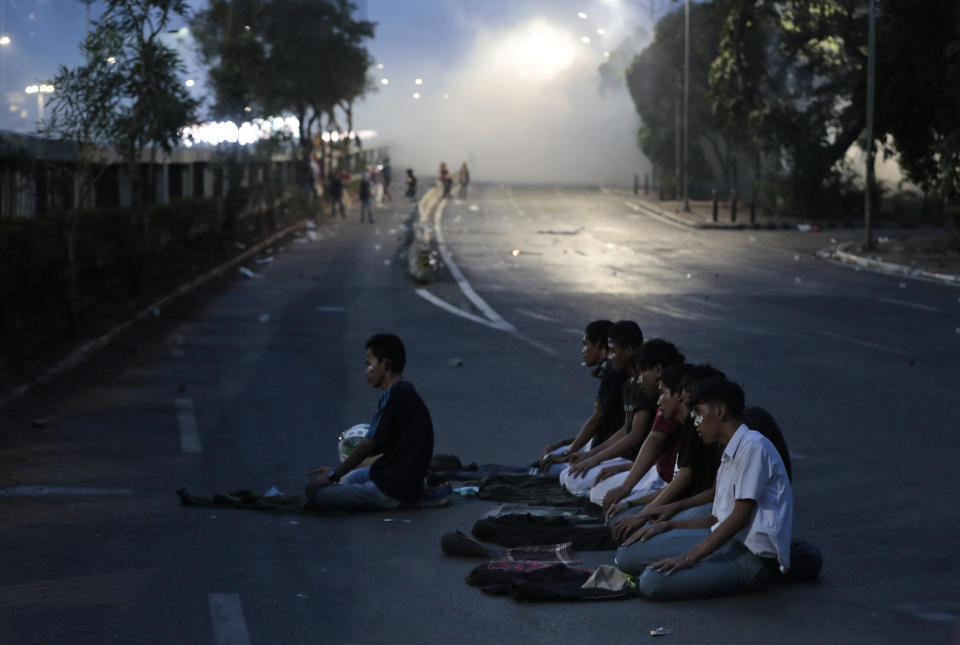 Muslim students perform an evening prayer as smoke from tear gas billows in the background during a clash with riot police in Jakarta, Indonesia, Monday, Sept. 30, 2019. Thousands of Indonesian students resumed protests on Monday against a new law they say has crippled the country's anti-corruption agency, with some clashing with police. (AP Photo/Dita Alangkara)