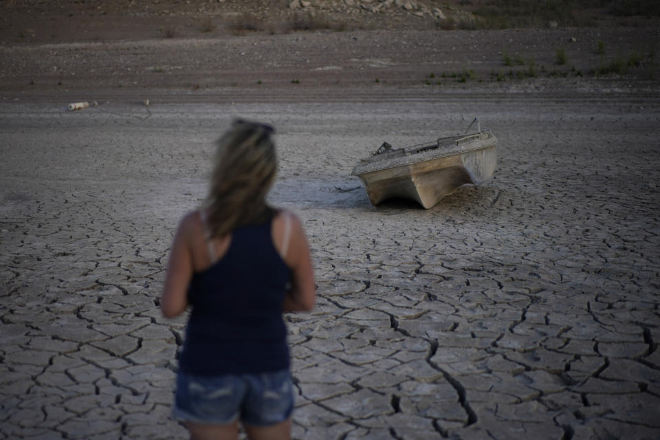 Misha McBride looks at a formally sunken boat now on cracked earth hundreds of feet from what is now the shoreline on Lake Mead at the Lake Mead National Recreation Area, Monday, May 9, 2022, near Boulder City, Nev. (AP Photo/John Locher)