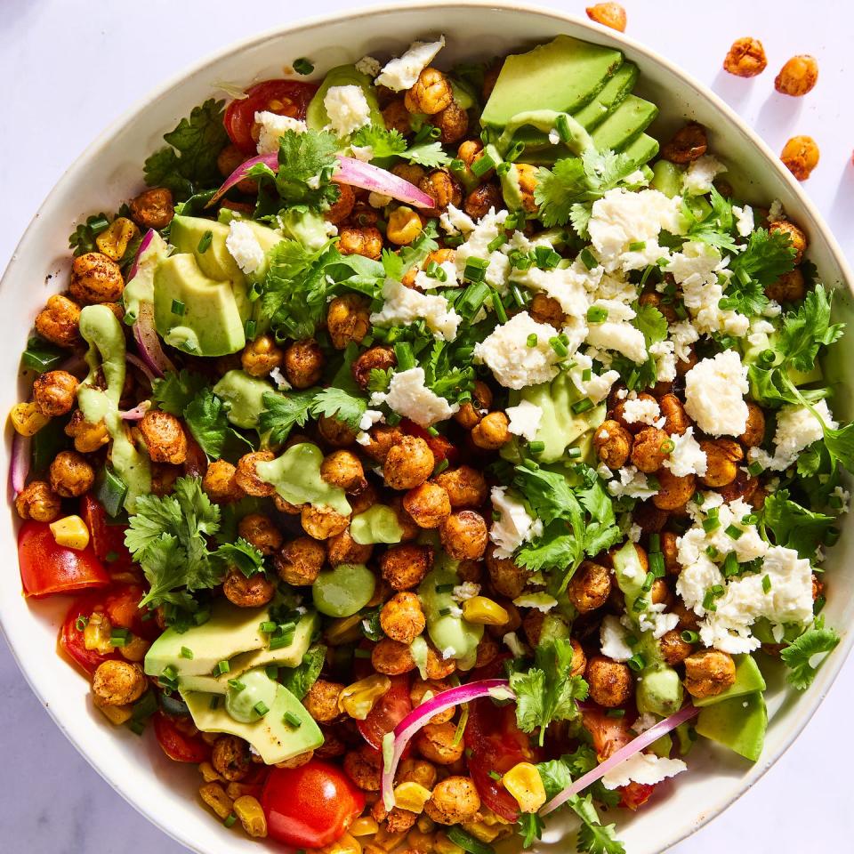 salad tossed with crispy chickpeas, avocado slices, red onions, sliced tomatoes, corn, and topped with herbs and cheese