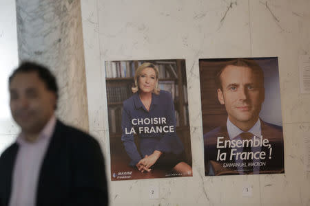 A poll worker stands next to posters for presidential candidates Marine Le Pen and Emmanuel Macron during the second round of the French presidential election at the French Consulate in New York, U.S. May 6, 2017. REUTERS/Joe Penney