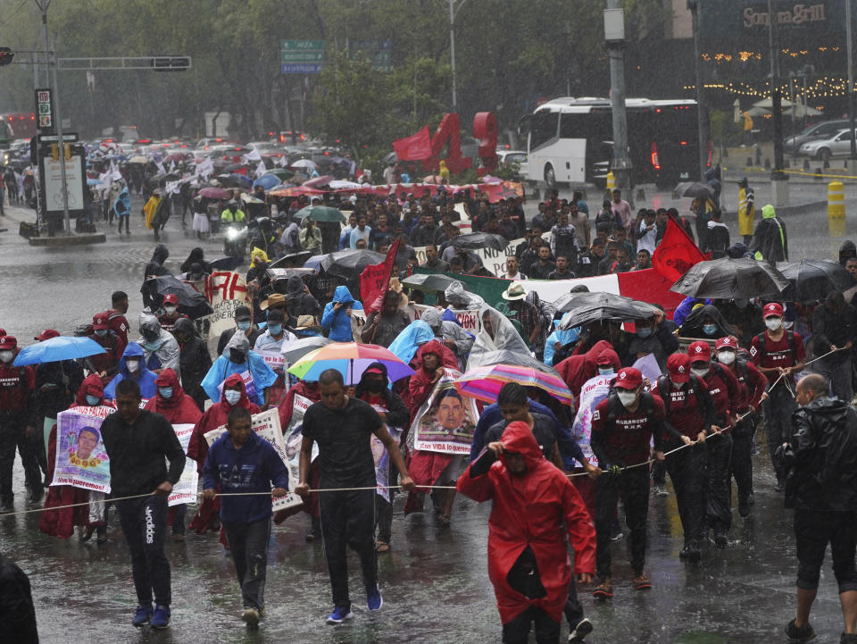 Friends and relatives seeking justice for the missing 43 Ayotzinapa students march in the rain in Mexico City, Friday, Aug. 26, 2022. Six of the 43 college students "disappeared" in 2014 were allegedly kept alive in a warehouse for days then turned over to the local army commander who ordered them killed, the Mexican government official leading a Truth Commission said Friday. (AP Photo/Marco Ugarte)