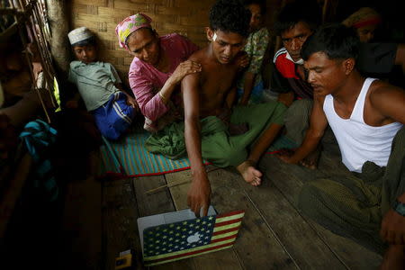 Abdhulami (C), 22, who was released from a human trafficking boat, points at pictures of people he recognises from the boat as he rests at a refugee camp outside Sittwe, Myanmar May 27, 2015. REUTERS/Soe Zeya Tun