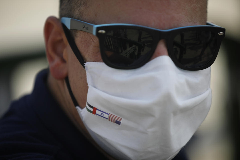 A man wearing a protective face mask with the national flags of America, Israel and United Arab Emirates looks on next to the Israeli flag carrier El Al's airliner which will carry Israeli and U.S. delegations to Abu Dhabi for talks meant to put final touches on the normalization deal between the United Arab Emirates and Israel, at Ben-Gurion International Airport, near Tel Aviv, Israel Monday, Aug. 31, 2020. (Nir Elias/Pool Photo via AP)