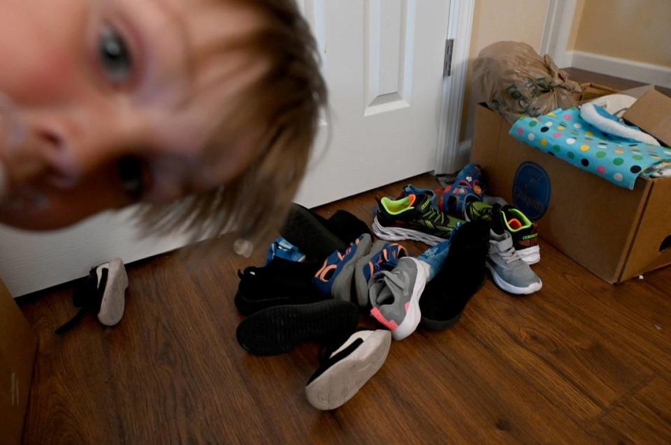 A young child curiously peers at the camera with a pile of shoes belonging to the foster children he shares his home with lay on the floor.