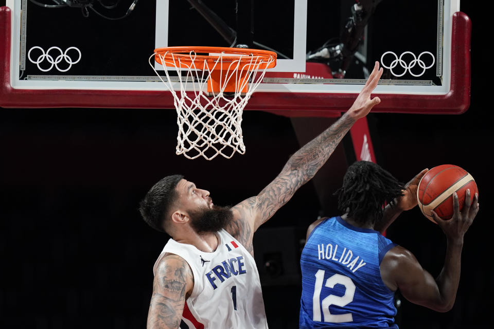 France's Vincent Poirier tries to block a shot by United States' Jrue Holiday (12) during a men's basketball preliminary round game at the 2020 Summer Olympics, Sunday, July 25, 2021, in Saitama, Japan. (AP Photo/Charlie Neibergall)