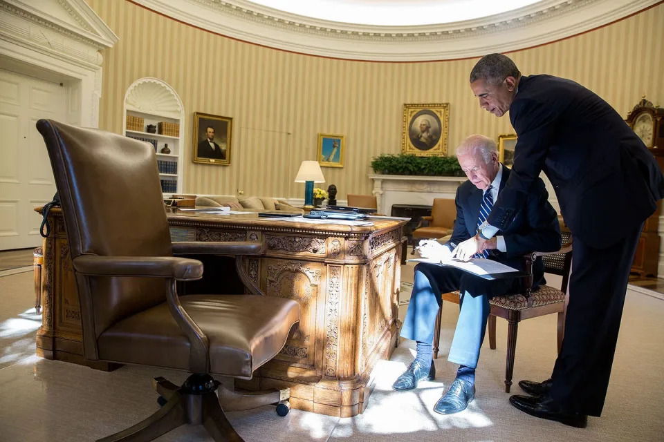 Joe Biden works on a speech in the Oval Office as Barack Obama stands over him giving pointers.