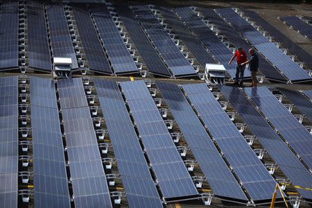 FILE PHOTO: Men gesture next to solar panels set up by Tesla, at the San Juan Children's Hospital, after the island was hit by Hurricane Maria in September, in San Juan, Puerto Rico October 26, 2017. REUTERS/Alvin Baez/File Photo