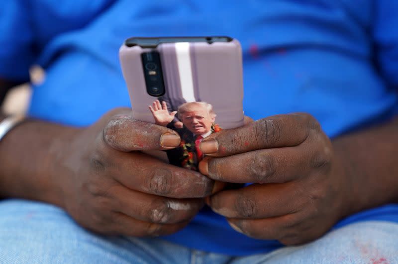 FILE PHOTO: Bussa Krishna, a fan of U.S. President Donald Trump, checks his mobile phone with an image of Trump outside his house in Konney village