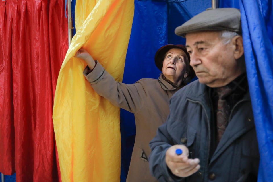 People exit voting cabins with curtains in the colors of the country's national flag in Bucharest, Romania, Sunday, Nov. 24, 2019. Romanians are voting in a presidential runoff election in which incumbent Klaus Iohannis is vying for a second term, facing Social Democratic Party leader Viorica Dancila, a former prime minister, in Sunday's vote. (AP Photo/Vadim Ghirda)