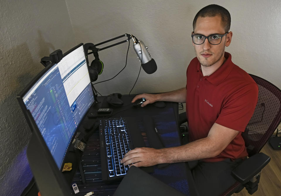 In this Sept. 20, 2021, photo Austin Moody poses for a photo as he sits a his home work station in Tampa, Fla. Moody, the Michigan native, got a scholarship from the Department of Defense that required working for the agency at least a year after graduating. Moody said he understands that state governments don't have the kind of money that federal agencies or private companies spend on recruiting and generous salaries. (AP Photo/Steve Nesius)